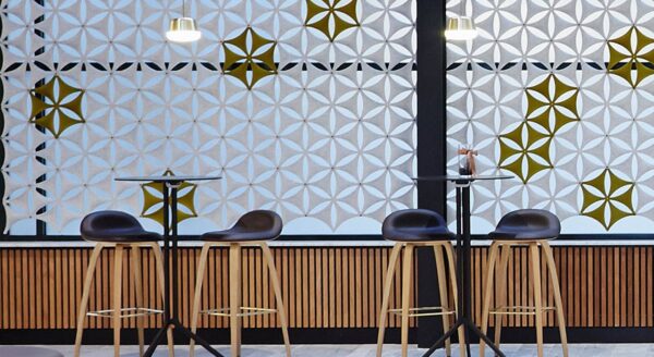Studio shot of two pairs of barstools placed in front of a set of Airflake acoustics. Backlit in white, olive colored Airflakes provide contrast with the matching white ones and surrounding decorations.