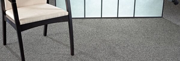 Studio shot of a Structure carpeting. A chair with a wooden frame is placed in front of a lit screen.