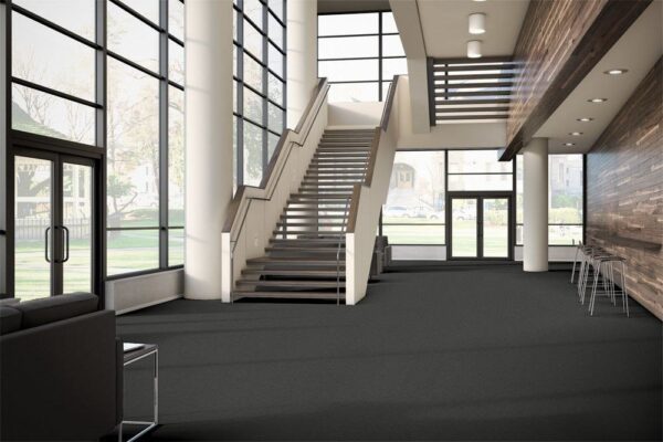 Tone model flooring on the floor of a company lobby. A long set of stairs leads upward. Tall backed chairs are placed along the wall, opposite the door.