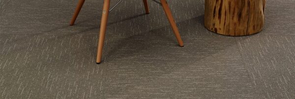 Studio photography of Tone carpeting, with a wooden end table and chair placed on top. Each square has been given a quarter turn for the design.