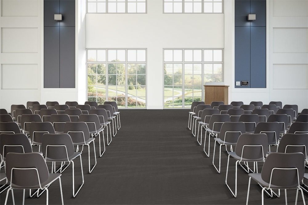 Flooring in a large lecture hall, using Transit's Gate color choice. A center aisle divides rows of medium backed metal framed chairs. Two windows in front look out to a grassy field.