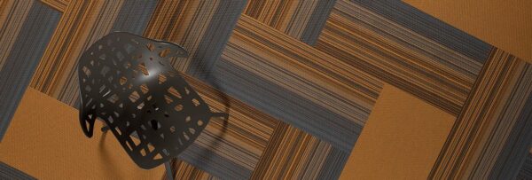 Studio shot of a dark grey plastic chair, resting on Umbra II carpeting. The carpet squares are arranged in a herringbone design. The chair's seat and back has been given a stylish cutout aesthetic.