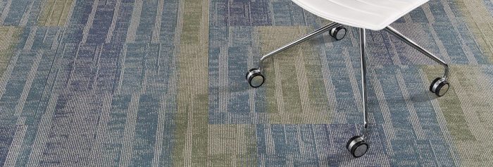 Studio shot of Well Versed model carpet, with palm greens and blues. A rolling office chair is cropped in from the top.